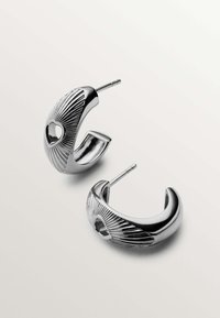 Pendientes de aro de plata con un diseño texturizado y acanalado, y un pequeño recorte en forma de corazón. Presentan un vástago recto para la inserción.