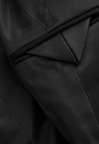 Gros plan sur un tissu noir avec un motif chevrons fin, plié pour mettre en valeur la texture et les détails de la couture.