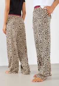 Pysjamasbukser med leopardmønster i beige med sorte prikker, med en rød elastisk talje, løs passform og sidelommer. Blødt stof.