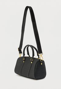 Musta, teksturoitu nahkalaukku, jossa on kahdet yläkahvat, irrotettava pitkä olkahihna ja kullanväriset metalliosat vaaleaa taustaa vasten.