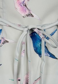 Světle šedá tkanina s barevnými potisky ptáků, má vázací pásek v pase, hladkou texturu a splývavý design.