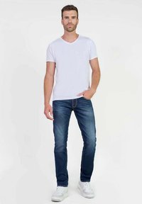 Camiseta blanca de cuello en V combinada con jeans de mezclilla azules. Los jeans tienen un ajuste clásico y un ligero desgaste, llevados con zapatillas blancas.