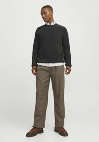 Pulover căptușit gri închis cu nervuri, cămașă albă cu guler dedesubt, pantaloni bej, pantofi maronii cu o talpă texturată. Design simplu și contemporan.