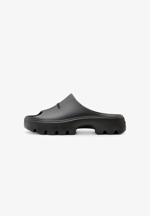 Schwarze Gummisandale mit konturiertem Fußbett, offenen Zehen und einer klobigen Sohle mit strukturiertem Griffmuster. Einfaches Design mit seitlichem Logo.
