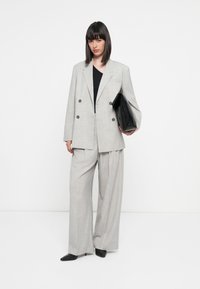 Grå dobbeltspent blazer med svarte knapper, matchende vide bukser og en svart clutch. Glatt stoff og avslappet passform.