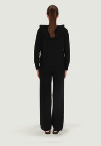 Czarna bluza z kapturem w luźnym kroju, z długimi rękawami, połączona z szerokimi czarnymi spodniami, wykonanymi z gładkiego, teksturowanego materiału.