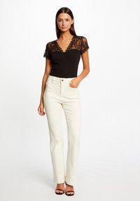 Bodysuit en dentelle noire à manches courtes, associé à un pantalon taille haute crème. Comprend des poches avant et une silhouette ajustée.