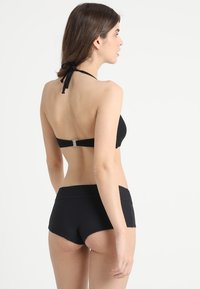 Zwarte bikini met een halternekontwerp en een gestructureerde afwerking. De top heeft een gestrikte sluiting, terwijl de onderkant hoog gaat en ribbels heeft.