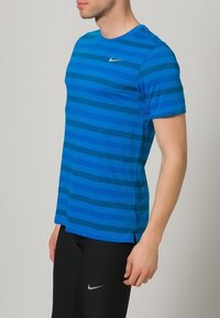 Sininen raidallinen lyhythihainen T-paita, joka on valmistettu teksturoidusta kankaasta ja jossa on pieni hopeanvärinen Nike-logo rinnassa, yhdistettynä mustiin urheiluhousuihin.