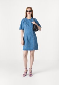 Denim dress with short sleeves, frayed hem, blue color, straight silhouette. Paired with a black handbag and purple strappy heels.