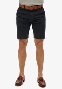 Marineblå bomuldsbukser med slim fit, der har et brunt læderbælte. Glat tekstur; lige kant. Fuldført med brune slip-on sko.