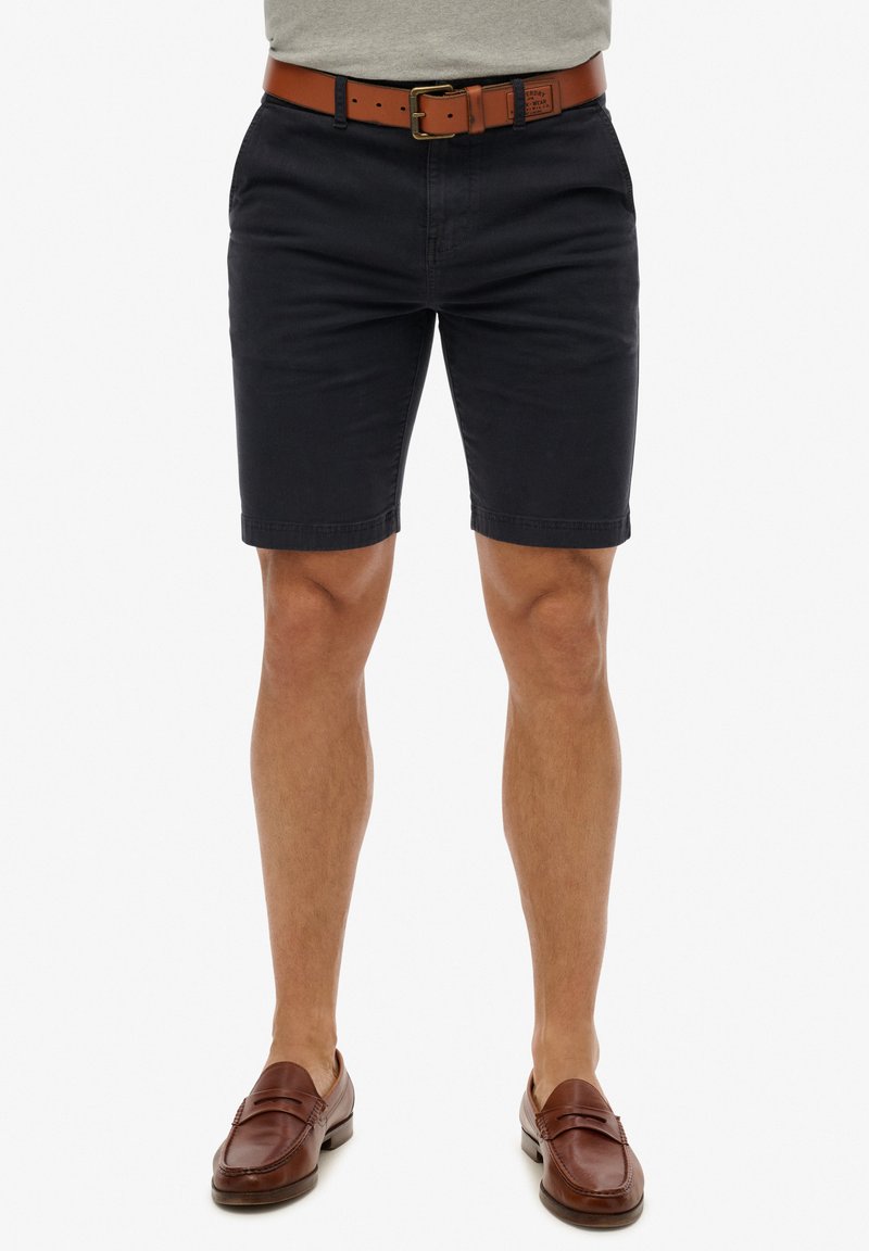 Marineblå bomuldsbukser med slim fit, der har et brunt læderbælte. Glat tekstur; lige kant. Fuldført med brune slip-on sko.