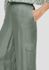 Lichtgroene satijnen broek met een relaxte pasvorm, voorzien van zijzakken en een opgestikte zak op het been. Gladde textuur en subtiele glans.