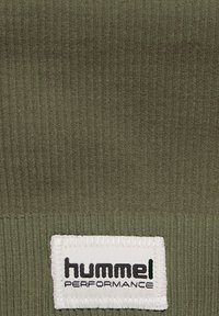 Grönt räfflat tyg med en vit etikett där "hummel PERFORMANCE" är sydd i svart, vilket framhäver textur och varumärkesidentitet.