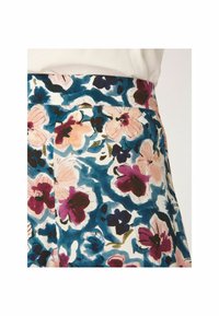 Gros plan d'une jupe taille haute avec un motif floral coloré en nuances de bleu, rose, violet et vert sur fond blanc.