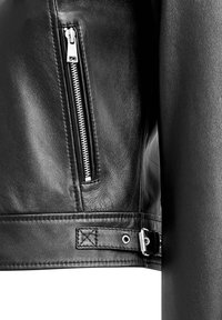 Dettaglio di giacca di pelle nera con tasca con zip in argento, texture liscia e cintura regolabile con fibbia in metallo sull'orlo.