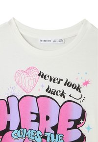 T-shirt bianca in cotone con scollo rotondo. Presenta un grafismo colorato con il testo: "non guardare mai indietro" e "Ecco che arriva..." in rosa e blu.