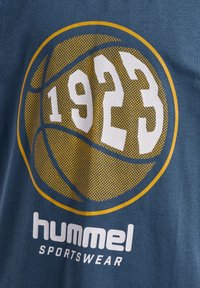 Blauwe katoenen t-shirt met een gele en witte basketball graphic waarop het jaar "1923" staat en de tekst "hummel SPORTSWEAR" eronder in het wit.