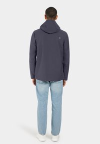 Marinblå huvtröja med en slät textur, med en subtil logo och långa ärmar, i kombination med ljusblå jeans och vita skor.