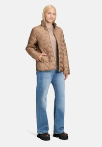 Brązowa pikowana kurtka z wysokim kołnierzem i zamkiem, z bocznymi kieszeniami. Połączona z jasnoniebieskimi dżinsami i ciemnymi butami na platformie.