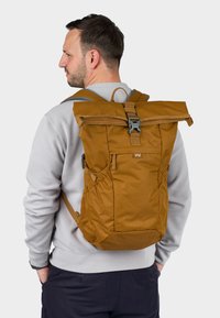 Zaino a forma di rotolo marrone con spallacci regolabili, tasche laterali e chiusura a clip. Realizzato in tessuto durevole con una consistenza liscia.