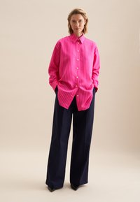 Roze gestreept overhemd met knopen en kraag, gecombineerd met marineblauwe wijde broek. Heeft lange mouwen en een relaxte pasvorm.