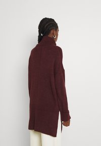 Maglione bordeaux lavorato a maglia con collo alto, maniche lunghe, orlo a coste e spacchi laterali, che presenta una finitura strutturata e una vestibilità rilassata.