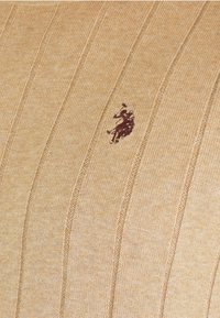 Material tricotat cu nervuri bej, având un mic logo brodat în maro închis reprezentând un jucător de polo călare.