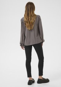 Grå blus med lång ärm och puffade axlar, parat med svarta skinnyjeans och kraftiga svarta skor. Enkelt mönster och slät textur.