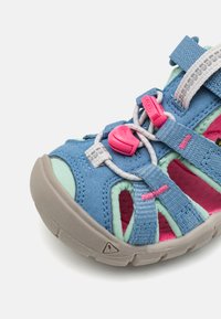 Blå och teal mockaskinnsandaler med nätutskärningar, rosa detaljer och elastiska snörningar med snörlås. Ljusgrå gummisula.
