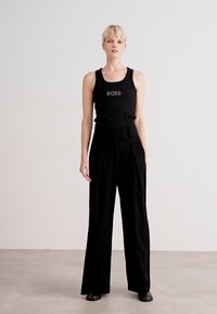 Top in tessuto nero senza maniche con logo "BOSS" in testo a contrasto abbinato a pantaloni neri a vita alta, in tessuto morbido e vestibilità sartoriale.