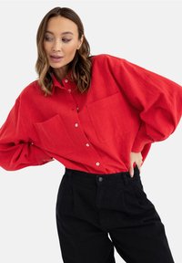 Czerwona, oversizowa koszula na guziki z dwoma kieszeniami na piersi, wykonana z teksturowanej tkaniny, zestawiona z czarnymi spodniami o wysokim stanie.