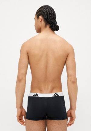 Schwarze Boxershorts mit einem weißen elastischen Bund, der drei schwarze Streifen aufweist, aus einem glatten Material, von hinten betrachtet.