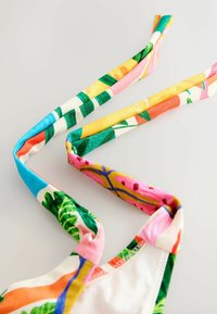 Kolorowe paski z tkaniny z tropikalnymi wzorami kwiatów i liści na białym tle, część ubrania lub dodatku.