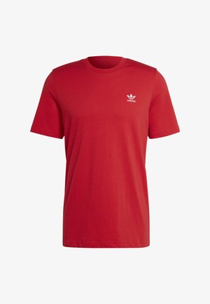 Punainen puuvillainen t-paita, jossa on pyöreä kaula-aukko ja valkoinen Adidas-logo, yhdistetty mustiin kapeneviin collegehousuihin ja mustiin lenkkareihin.