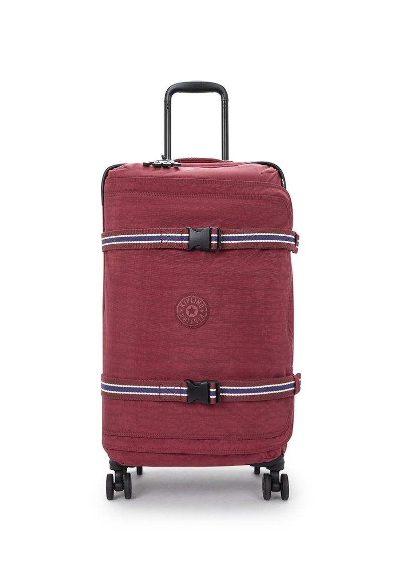 Red fabric suitcase with black wheels, extendable handle, and two adjustable straps. Features a circular logo in the center of the front.