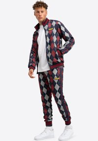 Rood en marineblauwe argyle trainingspak van gladde stof, met een zip-up jack en elastische manchetten, gecombineerd met witte sneakers.