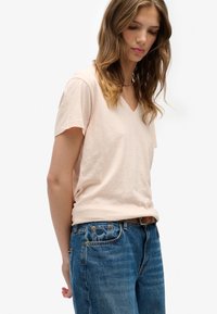 T-shirt rosa chiaro con scollo a V in un tessuto morbido e leggero; abbinata a jeans di jeans blu con leggero effetto sbiadito e cintura marrone.