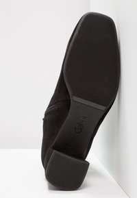 Czarne zamszowe botki za kostkę z płaską, teksturowaną gumową podeszwą, detalem w postaci suwaka po boku oraz minimalistycznym designem. Nazwa marki "Gabor" widoczna na podeszwie.