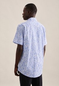Camicetta a maniche corte di colore azzurro chiaro con motivo paisley, dotata di un bordo curvo e colletto a punta, realizzata in tessuto leggero.