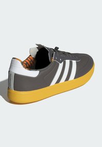 Chaussure de sport grise avec semelle jaune, rayures blanches et intérieure à motifs orange. Caractéristiques d'un dessus texturé et d'une languette rembourrée.