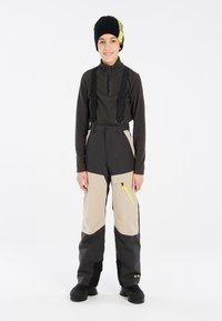 Pantalons de neige avec une palette de couleurs noir et beige, bretelles réglables et une poche zippée accentuée de jaune vif.