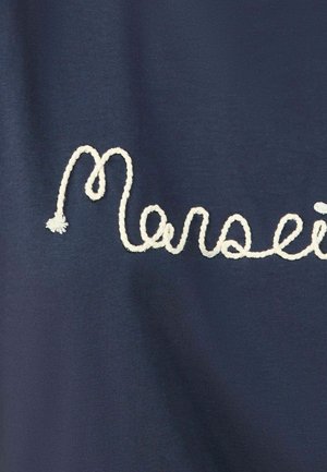 Jūras zilas audums ar izšūtu baltu kursīvu tekstu, kas raksta "Marseille". Virsma ir gluda ar mīkstu apdari.