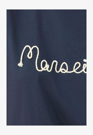 Jūras zilas audums ar izšūtu baltu kursīvu tekstu, kas raksta "Marseille". Virsma ir gluda ar mīkstu apdari.