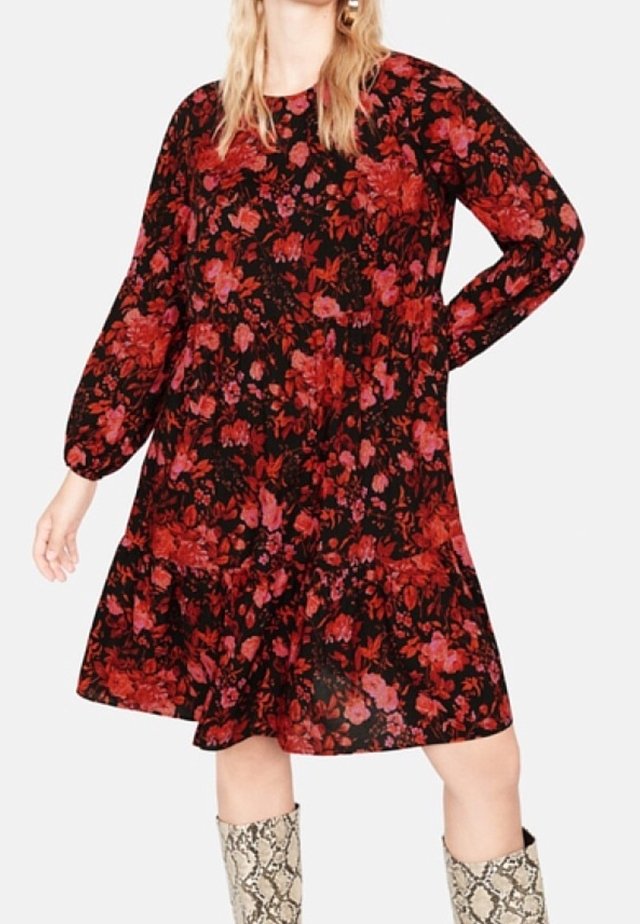 Robe noire avec imprimé floral rouge et rose, manches longues, col rond, taille froncée et ourlet évasé. Portée avec des bottes montantes à imprimé serpent.
