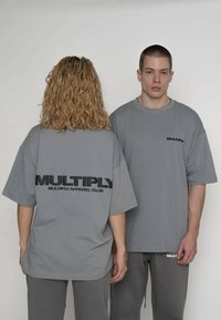 Grå oversize t-shirts med brandnavnet "MULTIPLY" fremtrædende vist på bagsiden i fed sort tekst. Blødt bomuldsmateriale.
