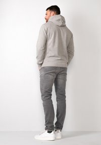 Grijze hoodie met een gladde textuur, strak design en kangoeroezak, gecombineerd met grijze slim-fit jeans en witte sneakers.