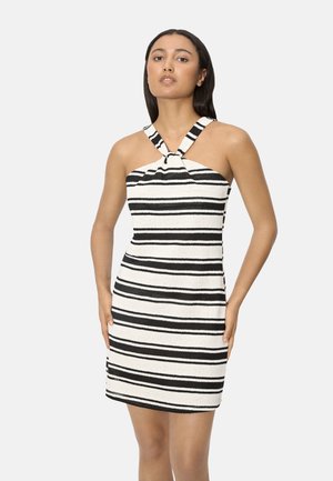 Mujer con un vestido sin mangas de rayas horizontales en blanco y negro, con un escote halter anudado, de pie contra un fondo liso.