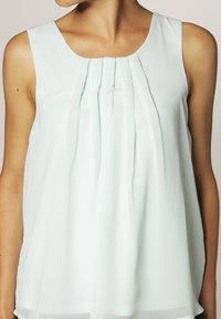 Blusa senza maniche verde menta chiaro con scollatura rotonda, caratterizzata da pieghe verticali sul davanti e una vestibilità ampia e fluida.