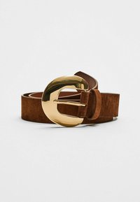 Ceinture en daim marron avec une grande boucle en métal doré brillant au design courbé, offrant une touche distinctive.
